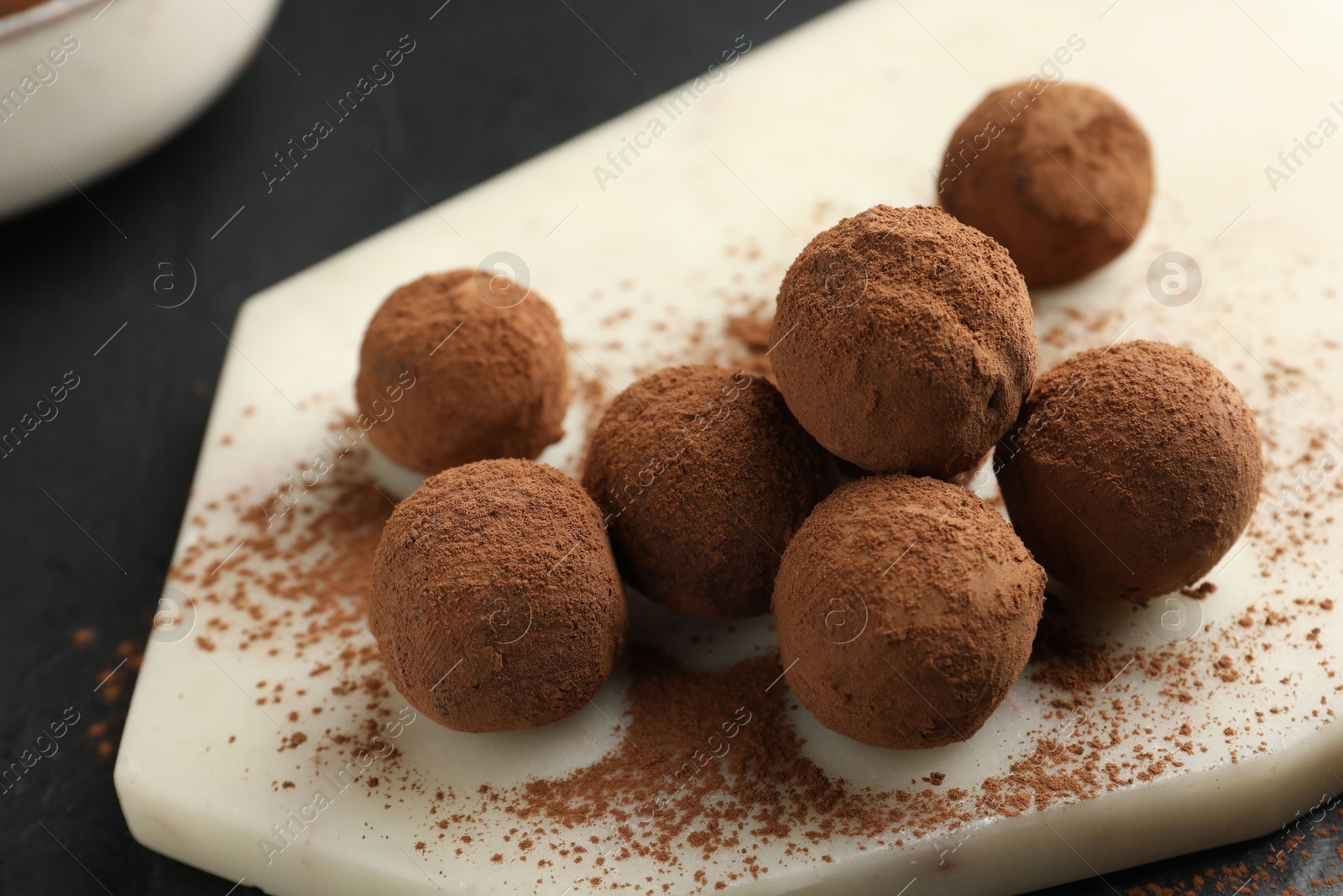 Tasty chocolate candies with cocoa powder on black table, closeup Photo of Tasty chocolate candies with cocoa powder on black table, closeup