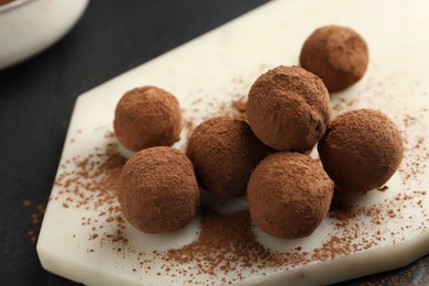 Photo of Tasty chocolate candies with cocoa powder on black table, closeup
