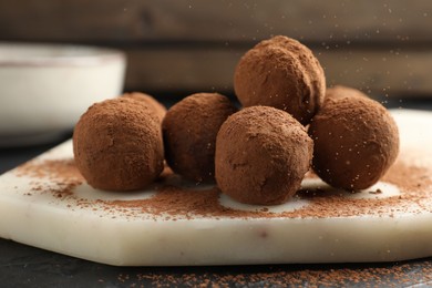 Photo of Tasty chocolate candies with cocoa powder on black table, closeup