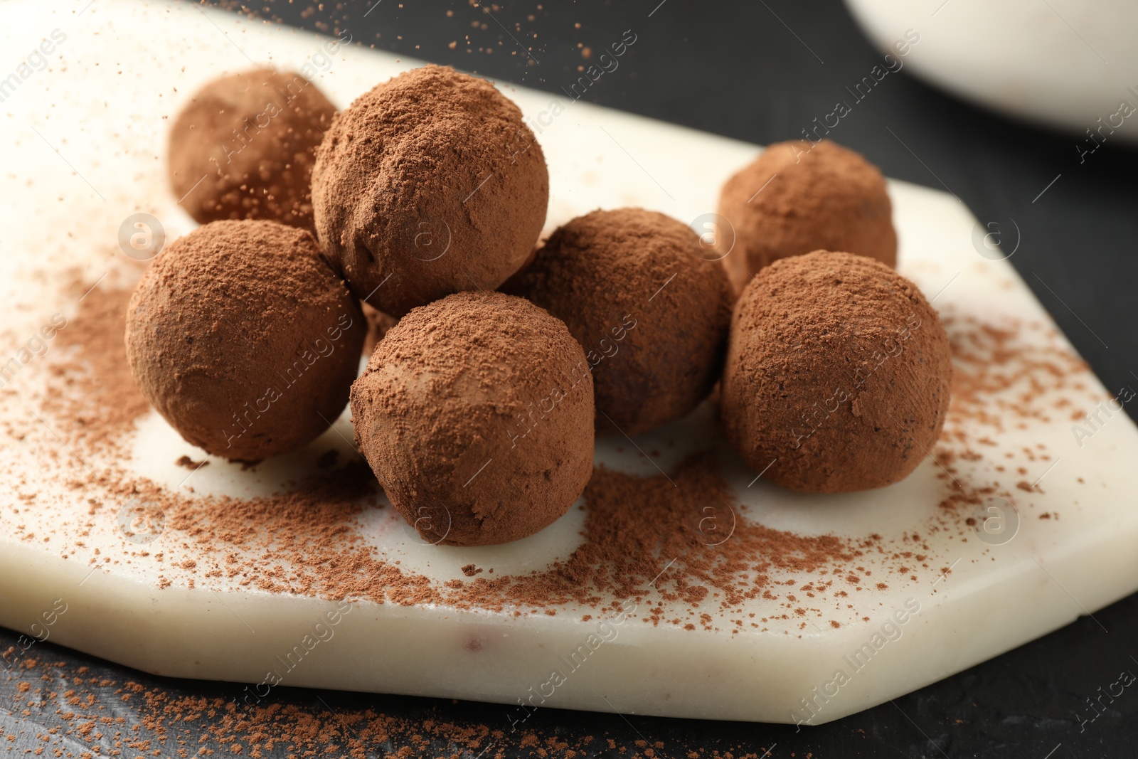 Tasty chocolate candies with cocoa powder on black table, closeup Photo of Tasty chocolate candies with cocoa powder on black table, closeup