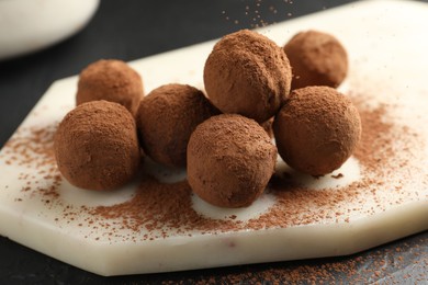 Photo of Tasty chocolate candies with cocoa powder on black table, closeup