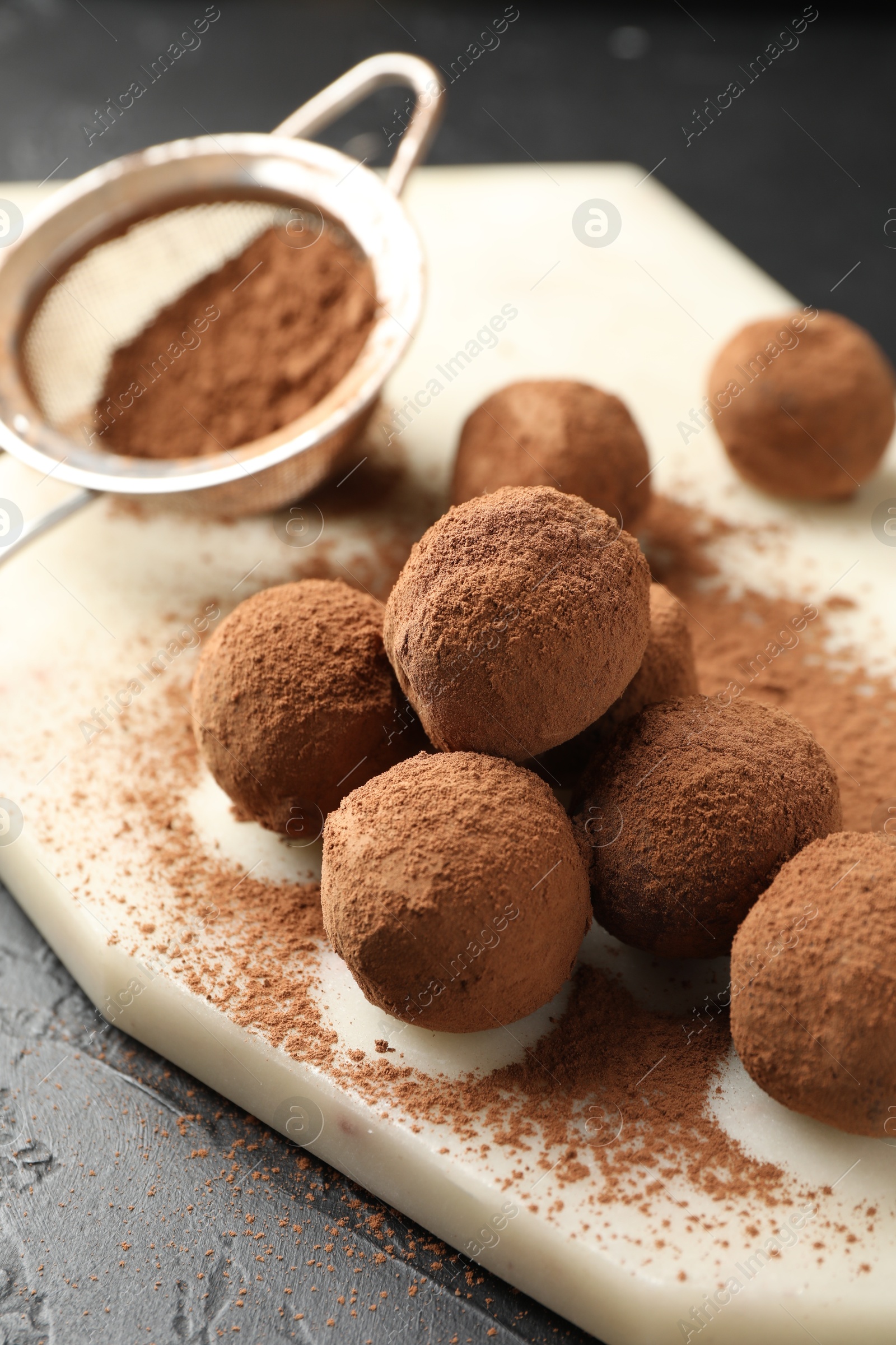 Tasty chocolate candies with cocoa powder on black table, closeup Photo of Tasty chocolate candies with cocoa powder on black table, closeup