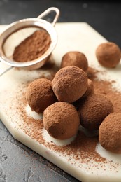Photo of Tasty chocolate candies with cocoa powder on black table, closeup