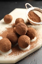 Photo of Tasty chocolate candies with cocoa powder on black table, closeup