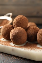 Photo of Tasty chocolate candies with cocoa powder on black table, closeup