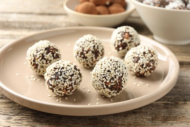 Photo of Tasty chocolate candies with nuts and sesame seeds on wooden table, closeup