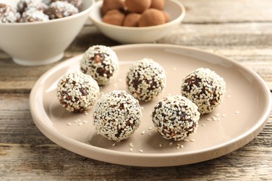Photo of Tasty chocolate candies with nuts and sesame seeds on wooden table, closeup
