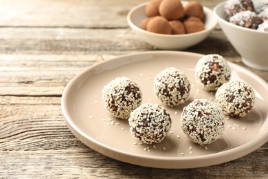 Photo of Tasty chocolate candies with nuts and sesame seeds on wooden table, closeup