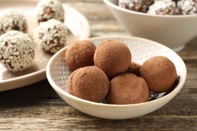 Photo of Tasty chocolate candies with cocoa powder, coconut flakes, nuts and sesame seeds on wooden table, closeup