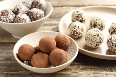 Photo of Tasty chocolate candies with cocoa powder, coconut flakes, nuts and sesame seeds on wooden table, closeup