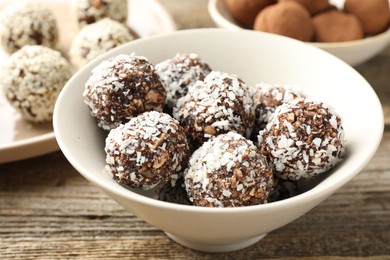 Photo of Tasty chocolate candies with coconut flakes, nuts, sesame seeds and cocoa powder on wooden table, closeup
