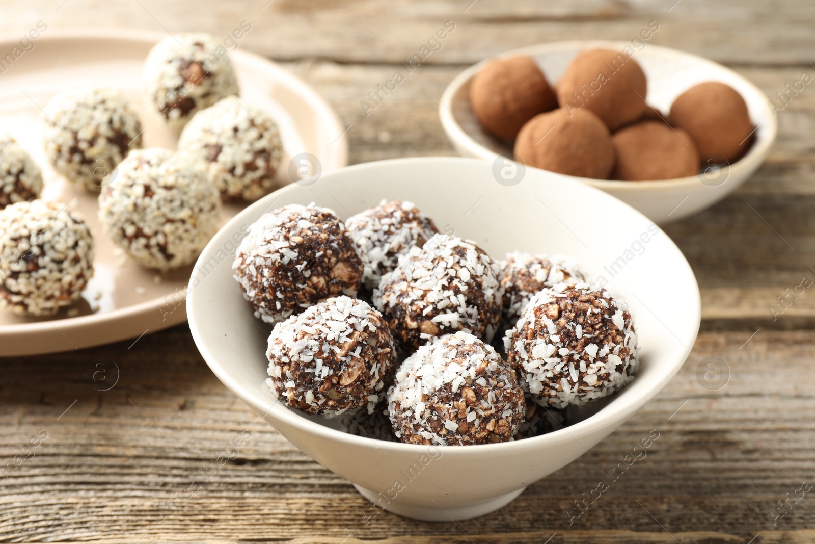 Tasty chocolate candies with coconut flakes, nuts, sesame seeds and cocoa powder on wooden table, closeup Photo of Tasty chocolate candies with coconut flakes, nuts, sesame seeds and cocoa powder on wooden table, closeup