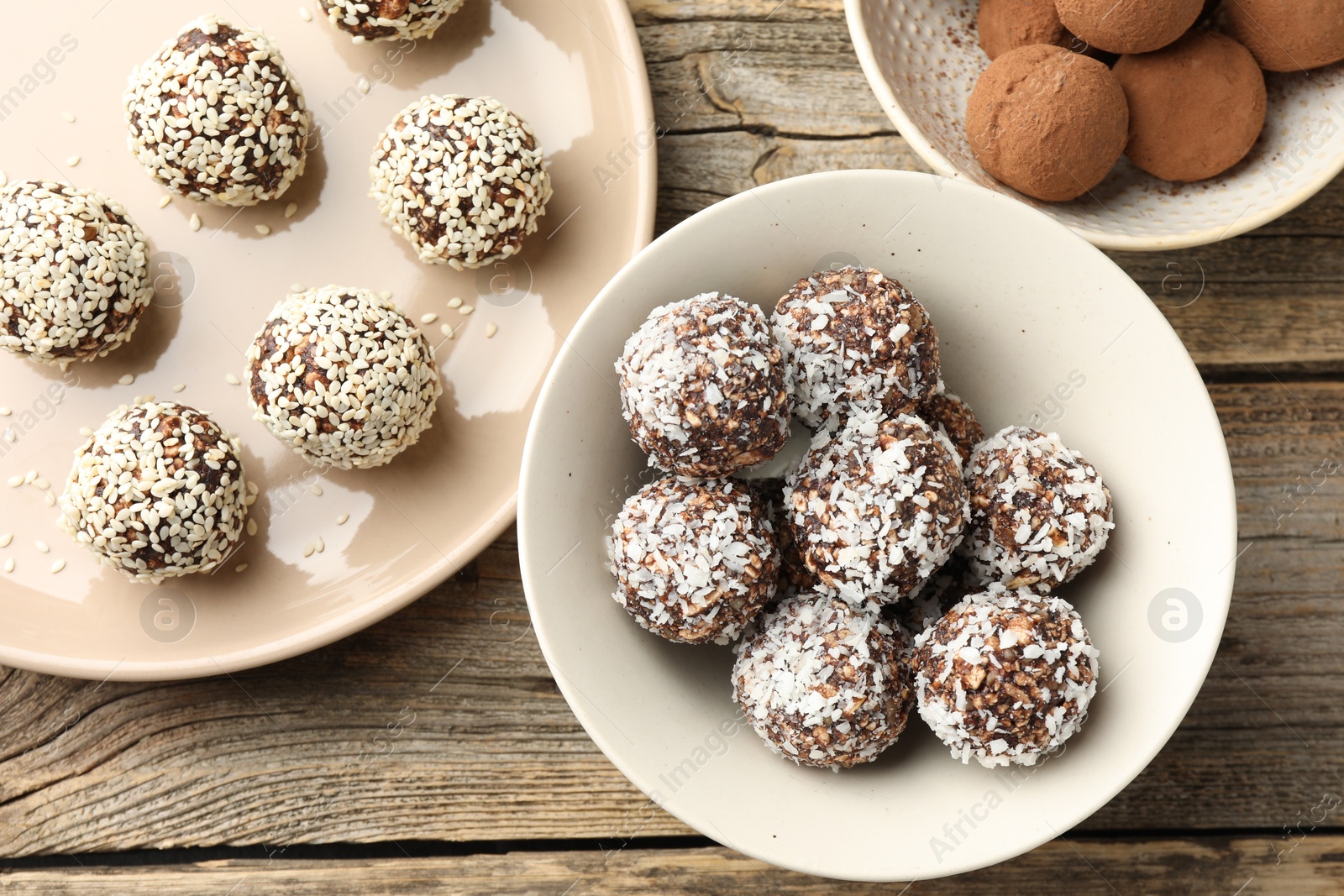 Tasty chocolate candies with coconut flakes, nuts, sesame seeds and cocoa powder on wooden table, flat lay Photo of Tasty chocolate candies with coconut flakes, nuts, sesame seeds and cocoa powder on wooden table, flat lay