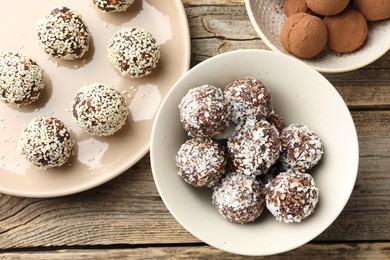 Photo of Tasty chocolate candies with coconut flakes, nuts, sesame seeds and cocoa powder on wooden table, flat lay
