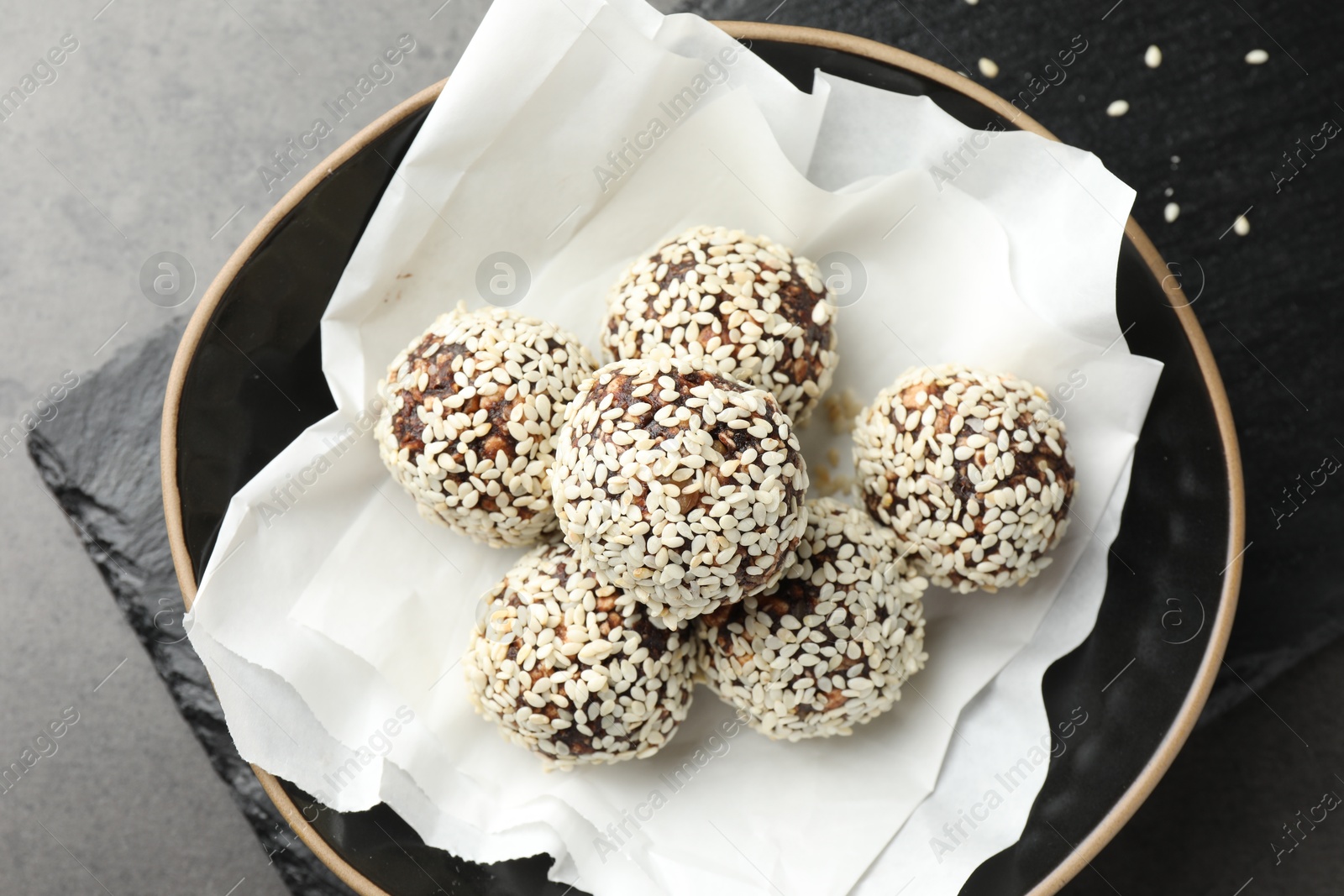 Tasty chocolate candies with nuts and sesame seeds in bowl on grey table, top view Photo of Tasty chocolate candies with nuts and sesame seeds in bowl on grey table, top view