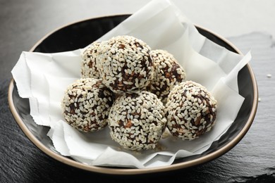Photo of Tasty chocolate candies with nuts and sesame seeds in bowl on table, closeup
