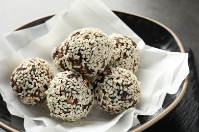 Photo of Tasty chocolate candies with nuts and sesame seeds in bowl on table, closeup