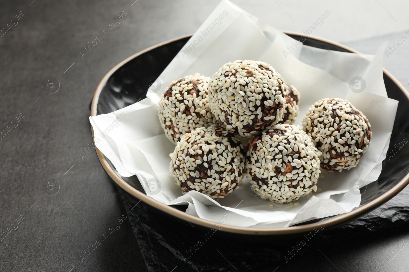 Tasty chocolate candies with nuts and sesame seeds in bowl on grey table, closeup Photo of Tasty chocolate candies with nuts and sesame seeds in bowl on grey table, closeup
