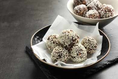 Photo of Tasty chocolate candies with nuts, sesame seeds and coconut flakes on grey table, closeup