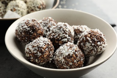 Photo of Tasty chocolate candies with nuts and coconut flakes in bowl on table, closeup