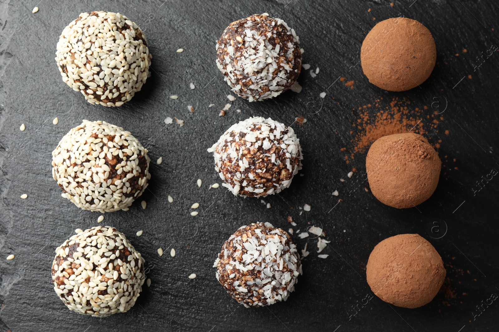 Tasty chocolate candies with cocoa powder, nuts, coconut flakes and sesame seeds on black table, flat lay Photo of Tasty chocolate candies with cocoa powder, nuts, coconut flakes and sesame seeds on black table, flat lay
