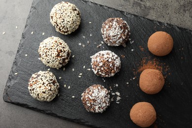 Photo of Tasty chocolate candies with cocoa powder, nuts, coconut flakes and sesame seeds on grey table, top view