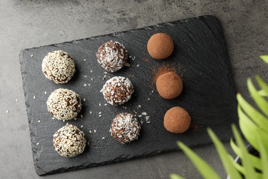 Photo of Tasty chocolate candies with cocoa powder, nuts, coconut flakes and sesame seeds on grey table, top view