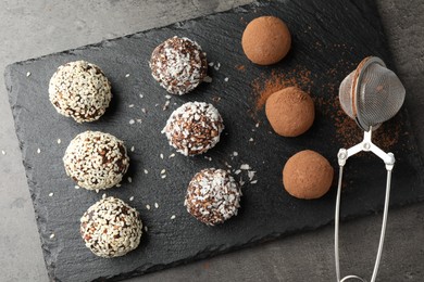 Photo of Tasty chocolate candies with cocoa powder, nuts, coconut flakes and sesame seeds on grey table, top view
