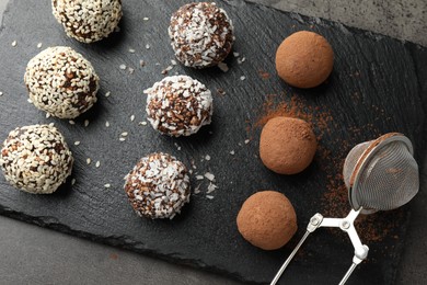 Photo of Tasty chocolate candies with cocoa powder, nuts, coconut flakes and sesame seeds on grey table, top view