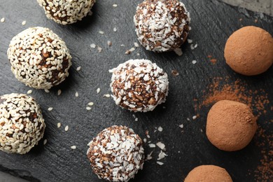 Photo of Tasty chocolate candies with cocoa powder, nuts, coconut flakes and sesame seeds on table, top view
