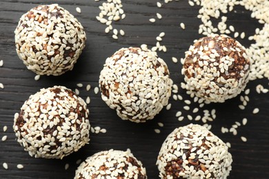 Photo of Tasty chocolate candies with nuts and sesame seeds on black wooden table, flat lay