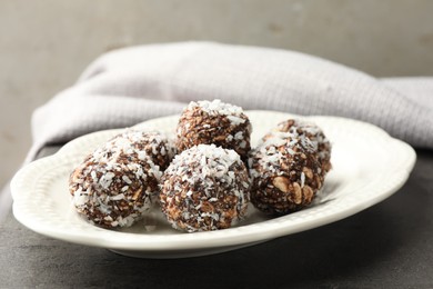 Photo of Tasty chocolate candies with nuts and coconut flakes on grey table, closeup