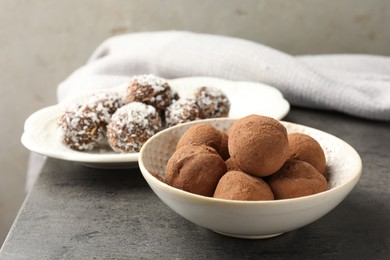 Photo of Tasty chocolate candies with cocoa powder, nuts and coconut flakes on grey table, closeup