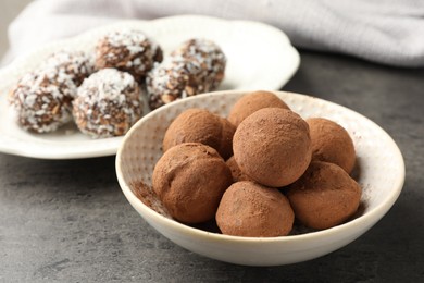 Photo of Tasty chocolate candies with cocoa powder, nuts and coconut flakes on grey table, closeup