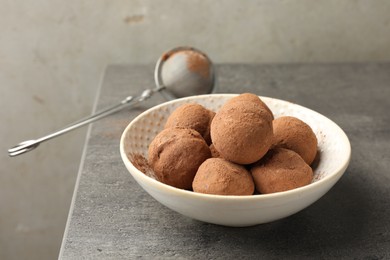 Photo of Tasty chocolate candies with cocoa powder in bowl on grey table, closeup