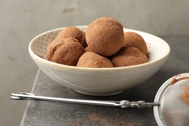 Photo of Tasty chocolate candies with cocoa powder in bowl on grey table, closeup