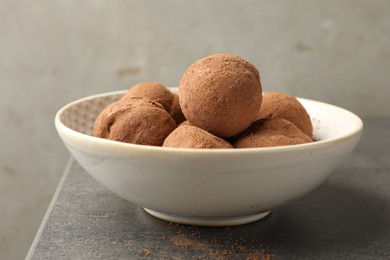 Photo of Tasty chocolate candies with cocoa powder in bowl on grey table, closeup