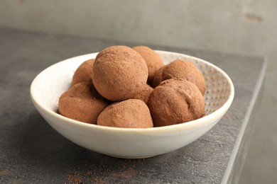 Photo of Tasty chocolate candies with cocoa powder in bowl on grey table, closeup