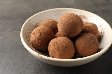 Photo of Tasty chocolate candies with cocoa powder on grey table, closeup