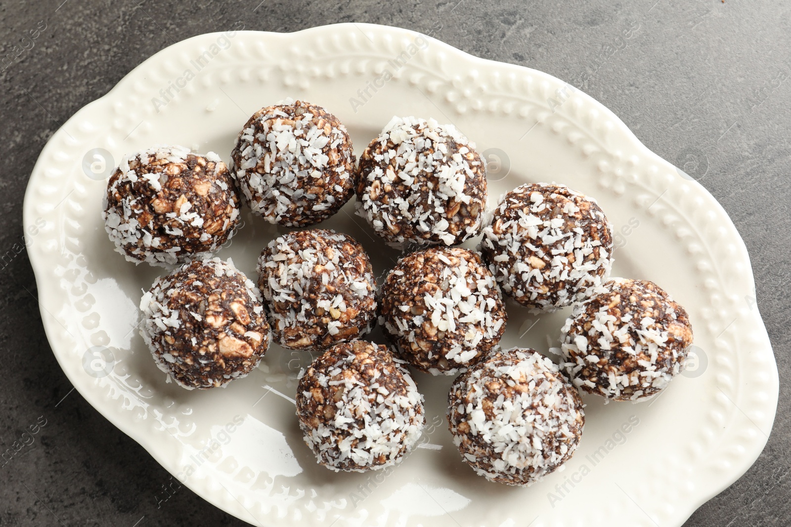 Tasty chocolate candies with nuts and coconut flakes on grey table, top view Photo of Tasty chocolate candies with nuts and coconut flakes on grey table, top view