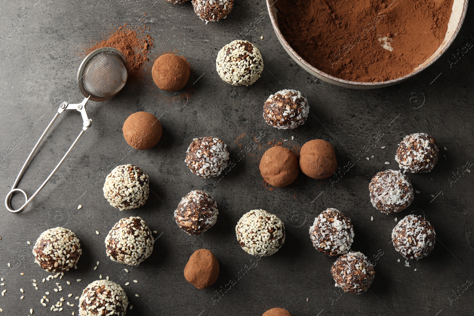 Tasty chocolate candies with cocoa powder, nuts, coconut flakes and sesame seeds on grey table, flat lay Photo of Tasty chocolate candies with cocoa powder, nuts, coconut flakes and sesame seeds on grey table, flat lay
