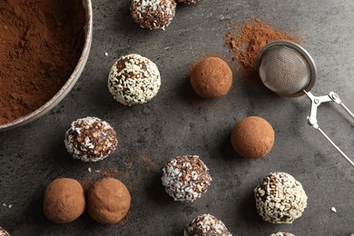 Photo of Tasty chocolate candies with cocoa powder, nuts, coconut flakes and sesame seeds on grey table, flat lay