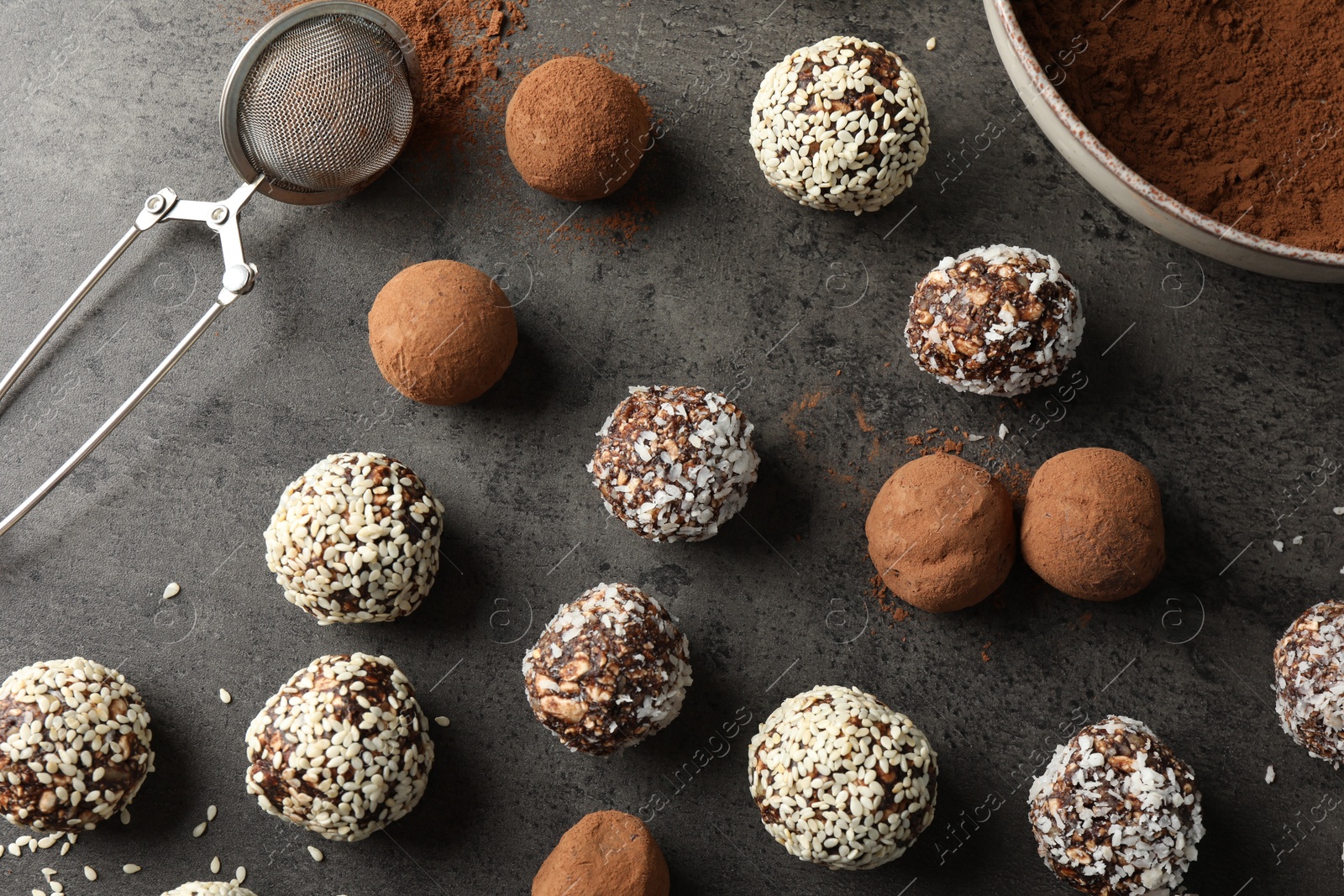 Tasty chocolate candies with cocoa powder, nuts, coconut flakes and sesame seeds on grey table, flat lay Photo of Tasty chocolate candies with cocoa powder, nuts, coconut flakes and sesame seeds on grey table, flat lay