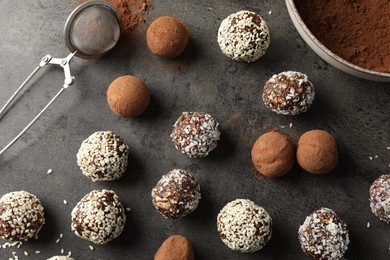 Photo of Tasty chocolate candies with cocoa powder, nuts, coconut flakes and sesame seeds on grey table, flat lay