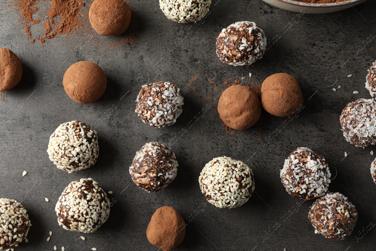 Tasty chocolate candies with cocoa powder, nuts, coconut flakes and sesame seeds on grey table, flat lay Photo of Tasty chocolate candies with cocoa powder, nuts, coconut flakes and sesame seeds on grey table, flat lay