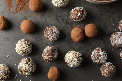 Photo of Tasty chocolate candies with cocoa powder, nuts, coconut flakes and sesame seeds on grey table, flat lay