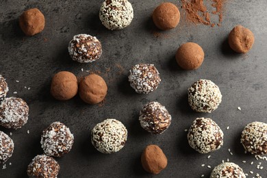 Photo of Tasty chocolate candies with cocoa powder, nuts, coconut flakes and sesame seeds on grey table, flat lay