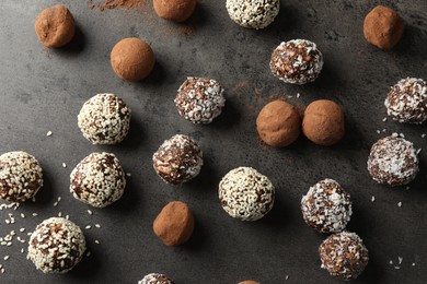 Photo of Tasty chocolate candies with cocoa powder, nuts, coconut flakes and sesame seeds on grey table, flat lay