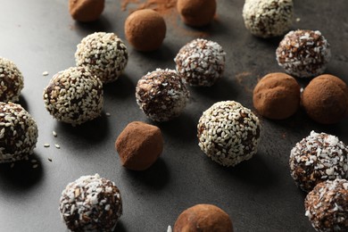 Photo of Tasty chocolate candies with cocoa powder, nuts, coconut flakes and sesame seeds on grey table, closeup