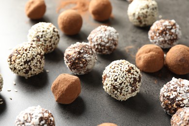 Photo of Tasty chocolate candies with cocoa powder, nuts, coconut flakes and sesame seeds on grey table, closeup